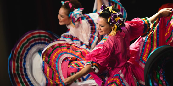 Colourful photo of 2 smiling dancers with their arms spread wide.